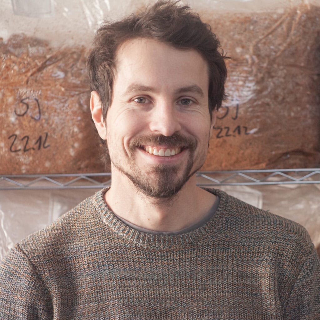 Martin Piringer mit Pilzen in der Pilzmanufaktur, lächelnd, im Hintergrund Pilzregale.